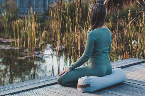 Woman in a yoga outfit meditationg in a sitting posture on a lakeside