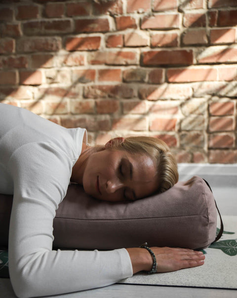 smiling woman in child's pose lying on a yoga bolster