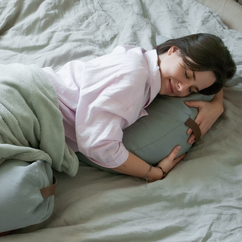 a woman sleeps in bed cuddling up to a grey moon pillow with a bolster between her legs
