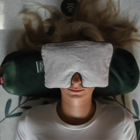 woman leaning her head against a green buckwheat roller while holding a lavender pillow over her eyes