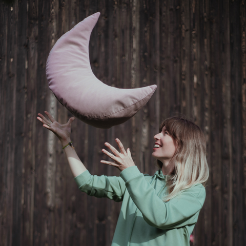 happy woman tossing a pink pillow in the shape of half a moon
