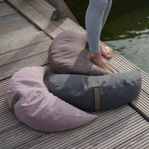 moon cushions from the be natural collection with linen and cotton covers in graphite, grey and pink are lying on the pier by the lake