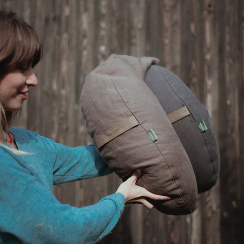 a woman holds in her hands against the background of a fence moon cushions from the natural collection in brown and graphite