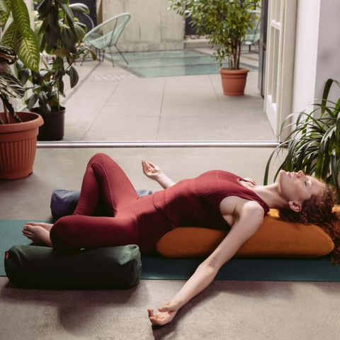 woman practising yoga on a mat with her back and head resting on an envelope pillow and her knees on small buckwheat rollers