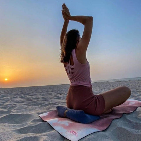 woman meditating on the beach at sunset while sitting on the blue wedge pillow 