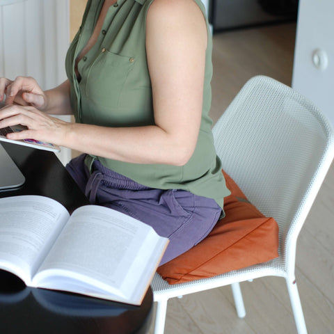 woman working remotely sitting in a chair with an orange wedge pillow