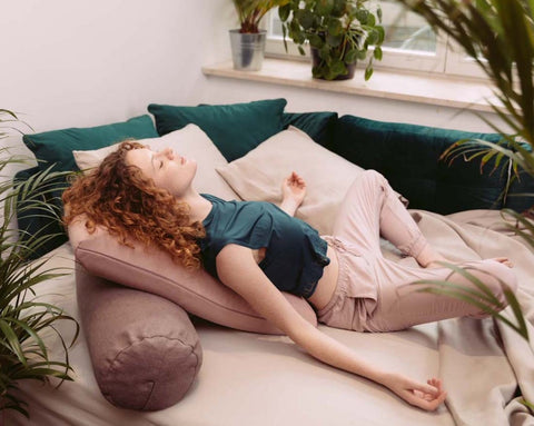 a woman relaxing on a bed resting her back on an envelope pillow and a yoga bolster