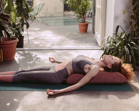 a woman practising yoga using a dark pink envelope pillow placed along her back