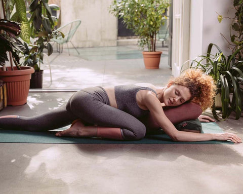 woman practising yoga by supporting her chest and head on an envelope pillow and a small buckwheat roller