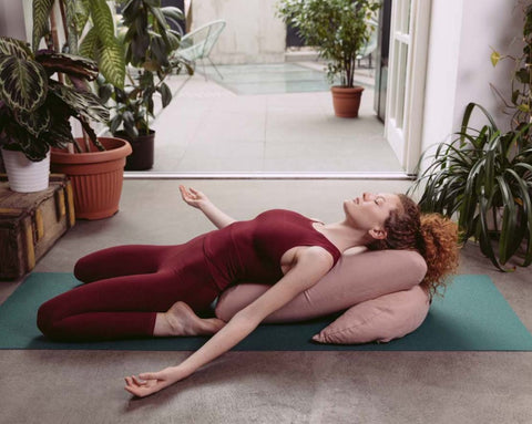 female yoga practitioner resting her back on an envelope pillow and a buckwheat moon pillow