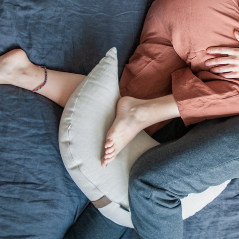 the legs of a couple relaxing on a sofa with a white moon cushion between their legs