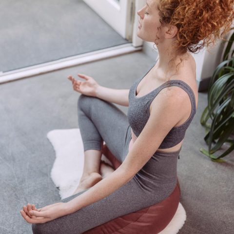woman meditates while sitting on a dark pink moon cushion