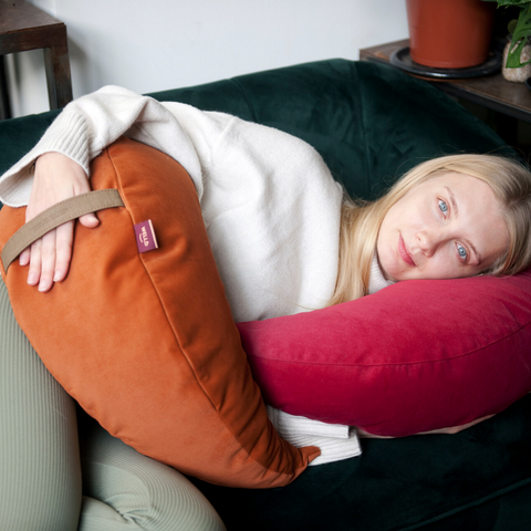 a woman lies on a sofa with a pink moon cushion under her head weighing down her body with an orange moon cushion
